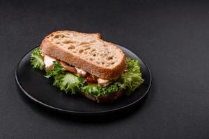 sanduíche saboroso fresco com frango, tomate e alface em um prato preto foto