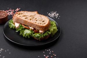 sanduíche saboroso fresco com frango, tomate e alface em um prato preto foto