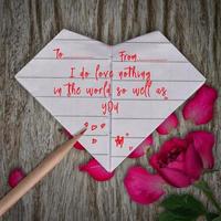 citações de amor em papel origami coração branco, lápis e flor rosa rosa no fundo da mesa de madeira foto