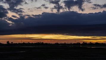 cenário de nuvens espessas flutuando sobre a silhueta de árvores e campos de arroz. foto