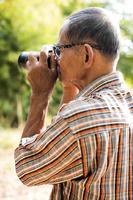 tiro lateral de um homem tailandês idoso usando óculos segurando uma câmera dslr antiga. foto