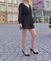 linda modelo loira vestindo um vestido preto curto e salto alto está tendo uma sessão de fotos na rua