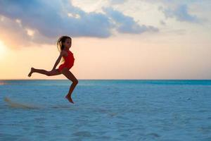 menina ativa pulando na praia branca ao pôr do sol foto