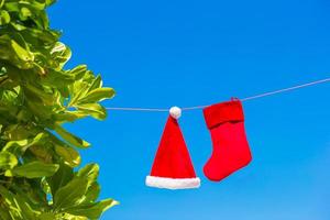 chapéu de papai noel vermelho e meia de natal entre palmeiras na praia branca foto