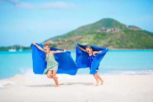 meninas bonitas se divertindo correndo com a toalha e aproveitando as férias na praia tropical com areia branca e água do mar turquesa foto