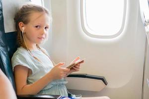 adorável menina viajando de avião. garoto bonito com laptop perto da janela em aeronaves foto