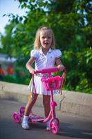 menina bonitinha alegre na scooter em um parque foto