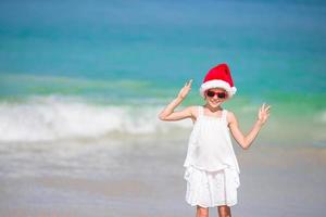 adorável menina com chapéu de Papai Noel em praia tropical foto