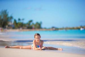 adorável menina deitada em águas rasas na praia branca foto