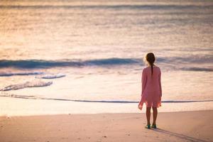 adorável menina feliz andando na praia branca ao pôr do sol. foto