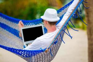 jovem com laptop na rede em férias tropicais foto
