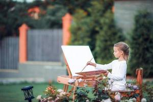 adorável menina pintando um quadro em um cavalete em um dia quente ao ar livre foto