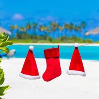 chapéus de papai noel vermelhos e meia de natal entre palmeiras na praia branca foto