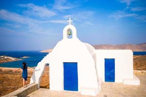 jovem e tradicional igreja branca com vista para o mar na ilha de mykonos, grécia foto