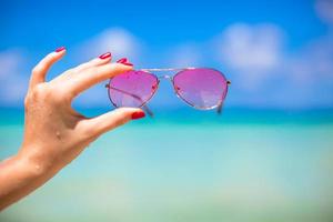 close-up de óculos de sol rosa coloridos na praia tropical foto