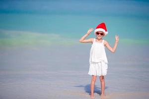 adorável menina com chapéu de Papai Noel em praia tropical foto