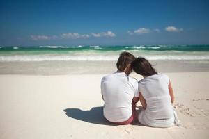 vista traseira do jovem casal na praia tropical branca foto