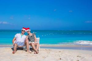 jovem casal feliz em chapéus de papai noel vermelhos na praia tropical foto