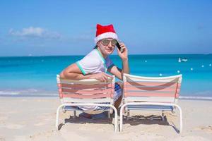 vista traseira do jovem com chapéu de natal na cadeira de praia foto