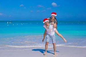 jovem casal feliz em chapéus de papai noel vermelhos durante suas férias tropicais foto