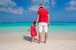 pai e filha com chapéu de Papai Noel na praia tropical foto
