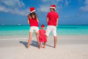 família feliz em chapéus de natal se divertindo na praia branca foto