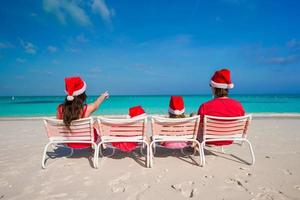 família feliz de quatro pessoas na praia com gorros vermelhos de papai noel foto