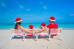 família de chapéu de Papai Noel se divertindo na praia tropical foto