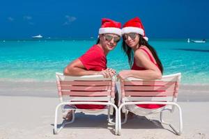 casal romântico feliz em chapéus de papai noel vermelhos na praia tropical foto