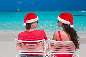casal romântico feliz em chapéus de papai noel vermelhos na praia tropical foto