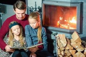 família lendo um livro juntos perto da lareira na véspera de natal foto
