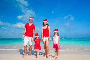 família de quatro pessoas em chapéus de Papai Noel se divertindo na praia tropical foto