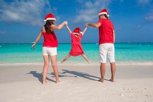 família feliz em chapéus de natal se divertindo na praia branca foto