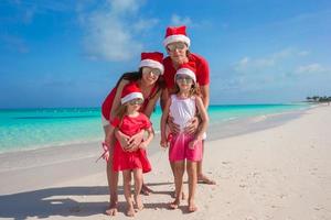 família feliz de quatro pessoas na praia com gorros vermelhos de papai noel foto