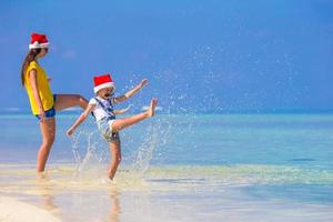 menina e jovem mãe com chapéu de Papai Noel durante as férias na praia foto