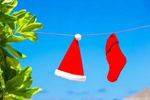 chapéu de papai noel vermelho e meia de natal pendurado na praia tropical entre palmeiras foto