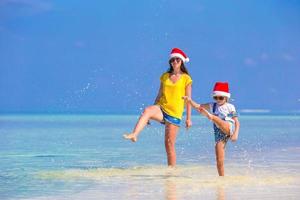 menina e jovem mãe com chapéu de Papai Noel durante as férias na praia foto