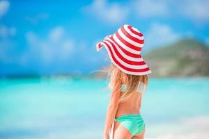 adorável menina de chapéu grande caminhando ao longo da praia de areia branca do Caribe foto