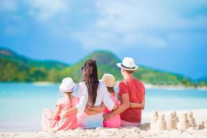 família de quatro pessoas fazendo castelo de areia na praia branca tropical foto