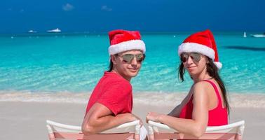 casal romântico feliz em chapéus de papai noel vermelhos na praia tropical foto