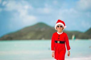 adorável menina com chapéu de Papai Noel em praia tropical foto