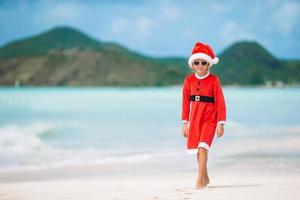 adorável menina com chapéu de Papai Noel em praia tropical foto