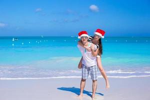 vista traseira do casal em chapéus de papai noel aproveite as férias na praia foto