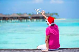 jovem de chapéu de Papai Noel na praia branca com miniatura de avião foto