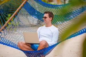 jovem com laptop na rede em férias tropicais foto