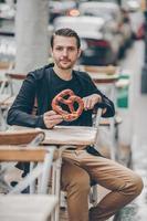 belo jovem segurando pretzel e relaxando no parque foto