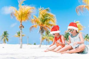 meninas adoráveis em chapéus de Papai Noel durante as férias na praia se divertem juntos foto