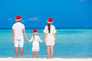 jovem família de chapéu de Papai Noel relaxando na praia tropical durante as férias de Natal