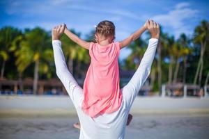 menina montando em seu pai andando na praia foto