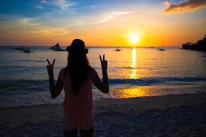 silhueta de uma jovem com as mãos levantadas ao pôr do sol na ilha boracay, filipinas foto